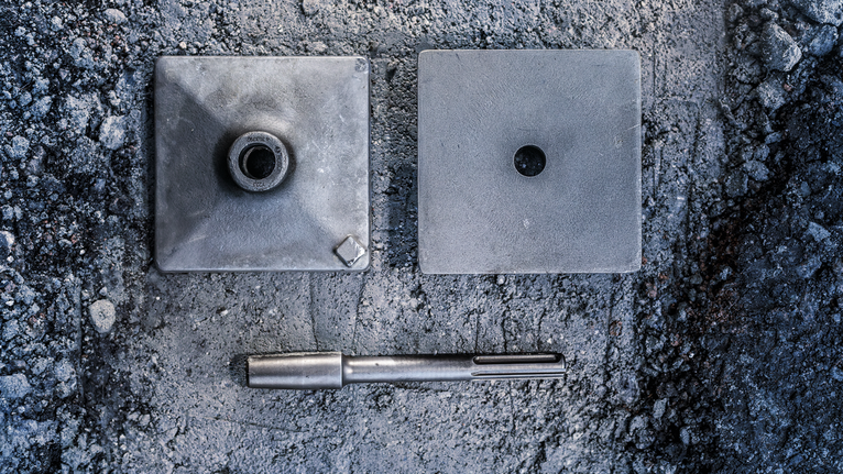 PRO SDS max Tamping Plate, 150 x 150 mm Metal core bit and two square mounting plates on a rough concrete surface.
