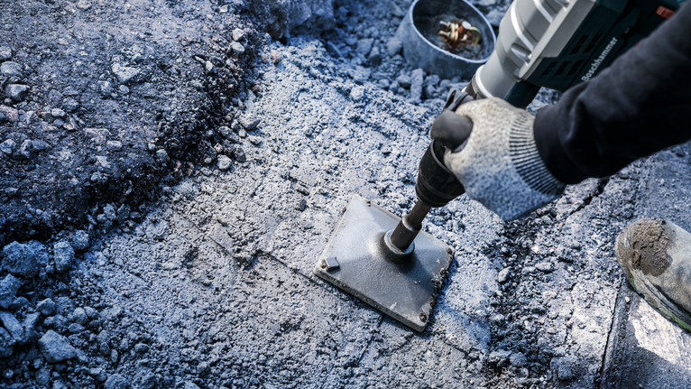 PRO SDS max Tamping Plate, 150 x 150 mm A person wearing safety equipment breaks concrete with a heavy-duty power tool.