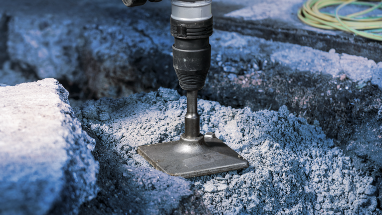 PRO SDS max Tamping Plate, 150 x 150 mm A power tool breaks through concrete with a flat chisel attachment.