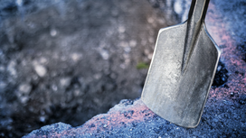 Shovel blade resting on rough concrete at the edge of a dug hole.