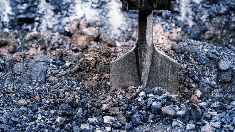 Chisel bit breaking up compacted gravel on a construction site.