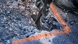 Demolition tool breaking asphalt within marked lines on a construction site.