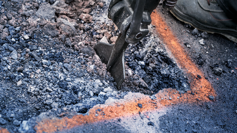 Demolition tool breaking asphalt within marked lines on a construction site.