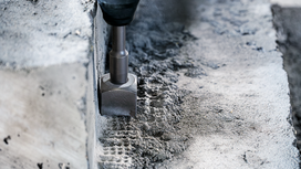Rotary hammer chisel breaking concrete surface.