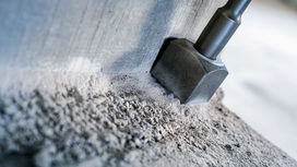 Chisel bit breaking concrete along a rough edge.