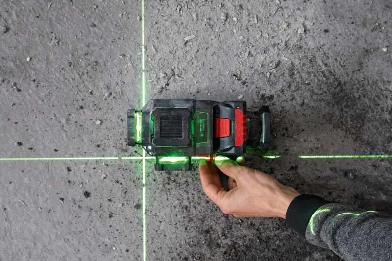 GLL 18V-120-33 CG A person adjusts a laser leveling tool projecting green lines on a concrete floor.