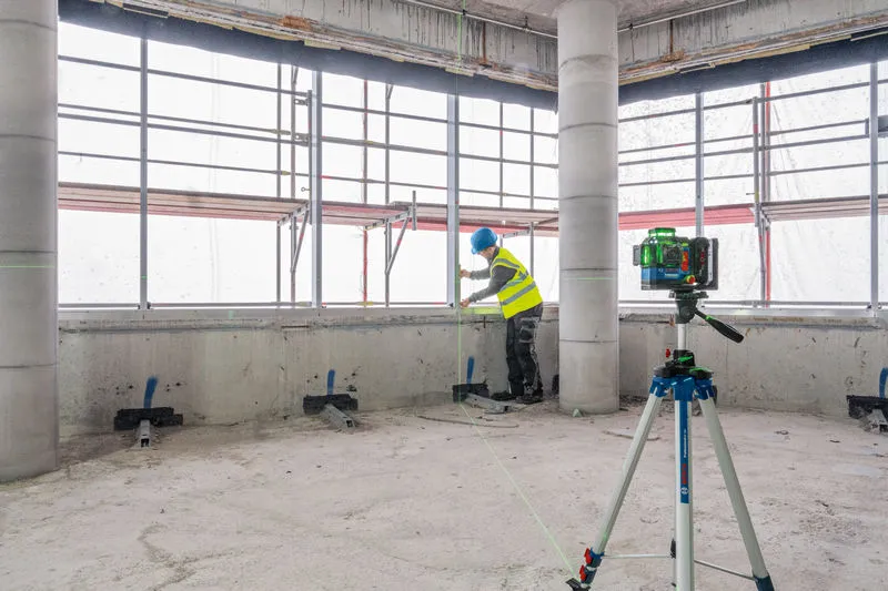 GLL 18V-120-33 CG Person wearing safety equipment aligns materials near a laser leveling tool on a tripod.
