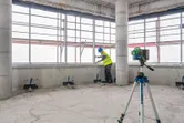 Person wearing safety equipment aligns materials near a laser leveling tool on a tripod.