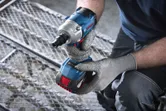 Person wearing safety equipment prepares to use a cordless impact wrench on metal grating.
