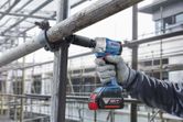 A person wearing safety equipment uses a cordless impact wrench to tighten scaffolding.