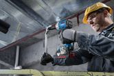 A person wearing safety equipment tightens a bolt on a metal beam using a cordless impact wrench.
