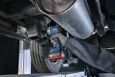 A person wearing safety equipment uses a cordless impact wrench on a vehicle undercarriage.