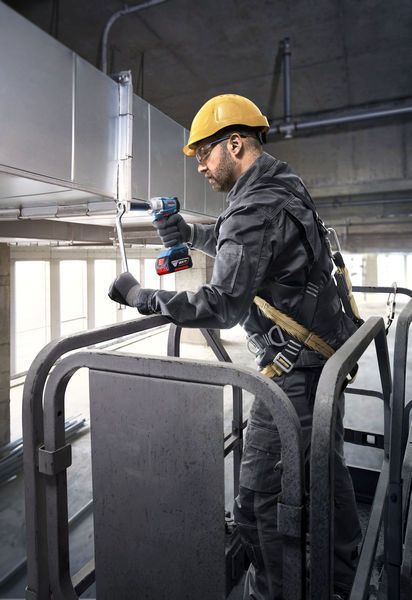 A person wearing safety equipment uses a cordless power tool to fasten ductwork.