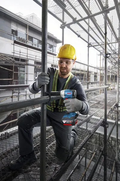 GDS 18V-350 + GSB 185 Combo A person wearing safety equipment tightens a pipe joint with a cordless impact wrench on scaffolding.