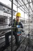 A person wearing safety equipment uses a cordless impact wrench on scaffolding.