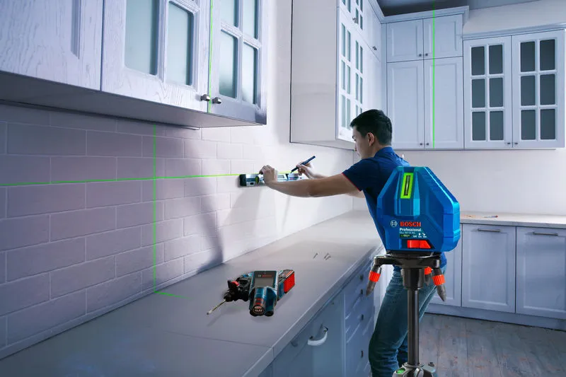 A person uses a laser leveling tool to align cabinets in a kitchen.
