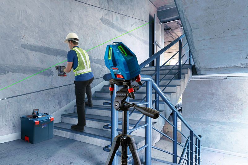 A person wearing safety equipment drills into a stairwell wall using a laser leveling tool.