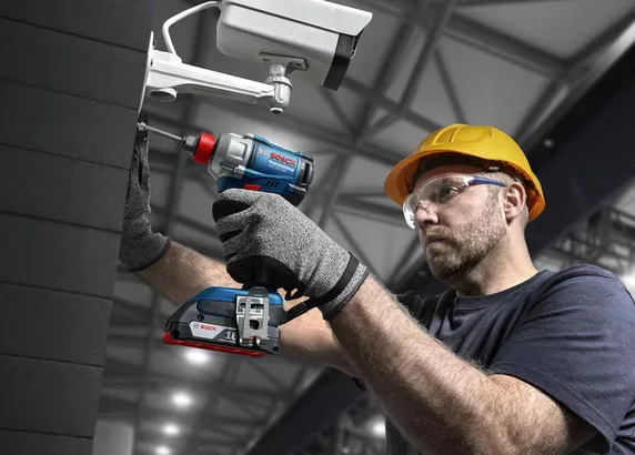 Professional Promotion Set of Combo GDX 18V-285 + GSB 185-LI with 2x2.0Ah, GAL 18V-20 in Case A person wearing safety equipment uses a cordless drill to install a security camera.