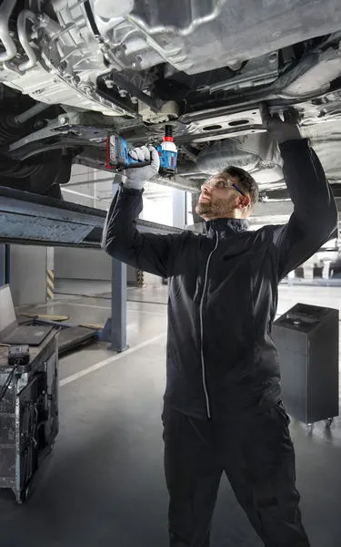 GDX 18V-285 A person wearing safety equipment uses a cordless drill under a lifted vehicle.