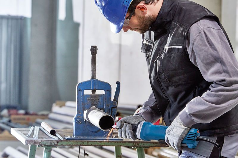 A person wearing safety equipment uses a straight grinder to work on a metal pipe.