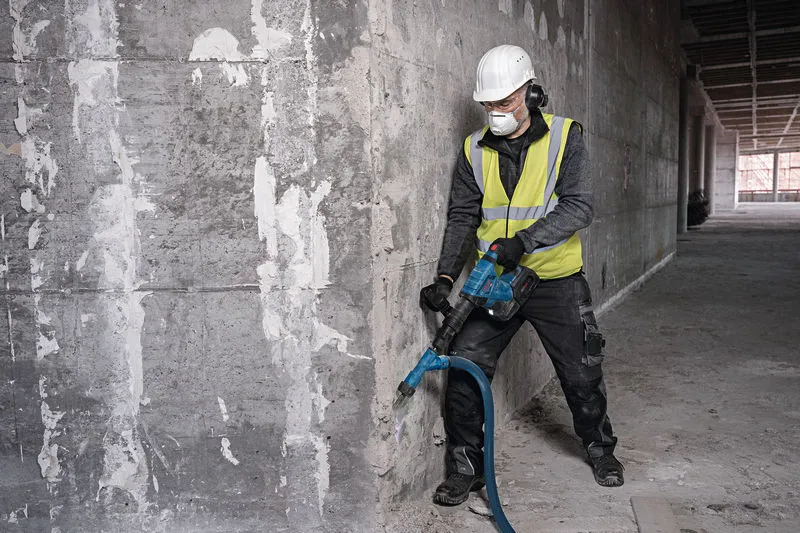 GSH 18V-5 A person wearing safety equipment breaks concrete with a cordless demolition hammer.
