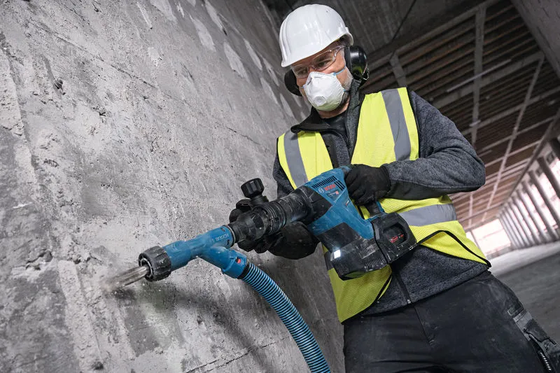 GSH 18V-5 A person wearing safety equipment uses a cordless demolition hammer on a concrete wall.