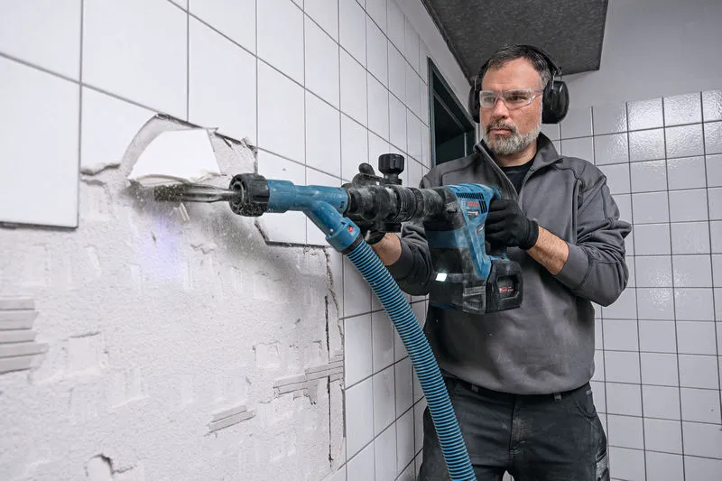 GSH 18V-5 A person wearing safety equipment uses a cordless demolition hammer to break wall tiles.