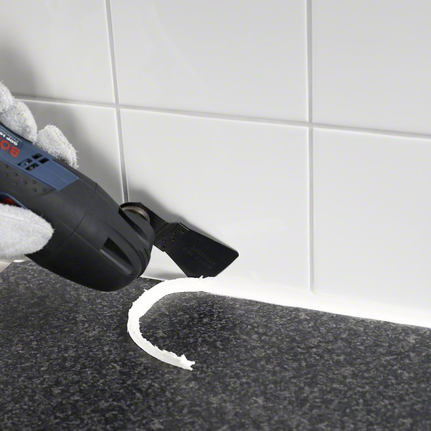 HCS scraper ATZ 52 SFC, flexible Gloved hand uses a multitool to remove silicone sealant from a tiled surface.