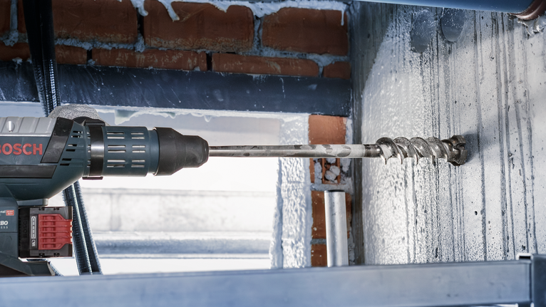Rotary drill boring a hole into a concrete wall indoors.