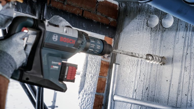 A person wearing safety equipment drills into a concrete ceiling.