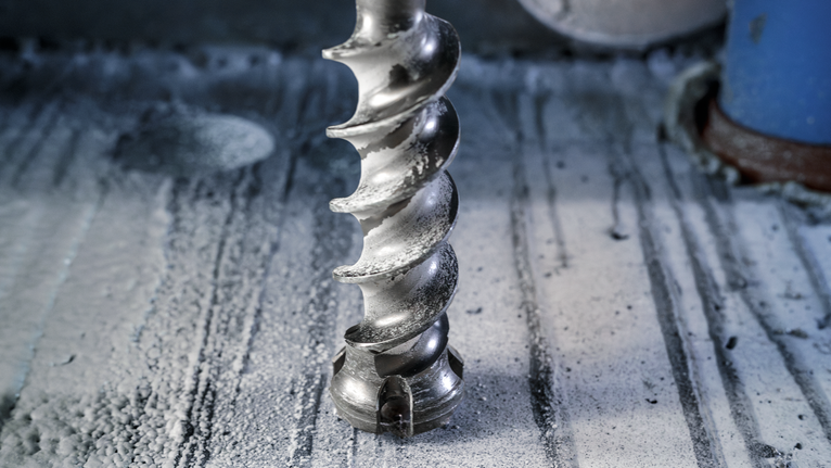 Large auger drill bit making a hole in a concrete surface.