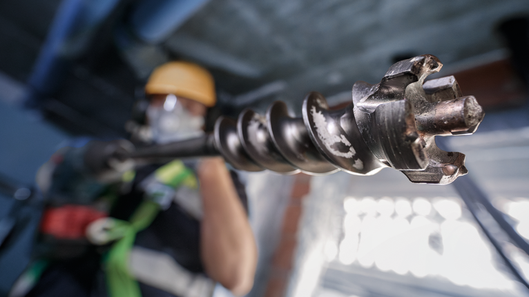 A person wearing safety equipment operates a large rotary drill bit.