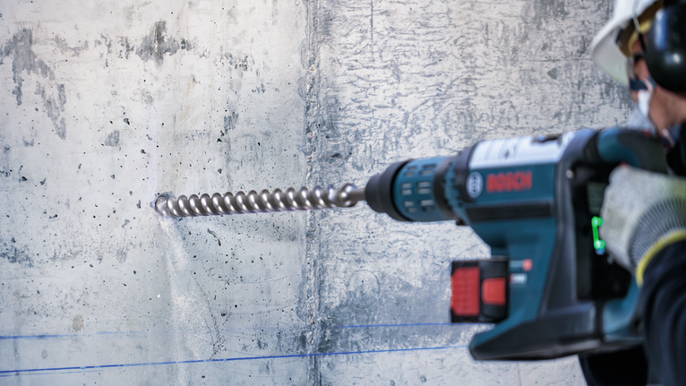 PRO SDS-max-7 Drill Bit, 35x400x520 mm Person wearing safety equipment drills into a concrete wall with a rotary hammer.