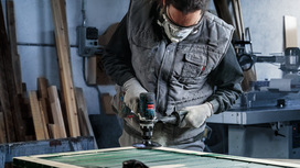Person wearing safety equipment polishes a wooden surface with a power tool.