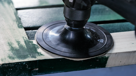 Rotary sander smoothing a wooden plank.