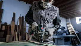 Person wearing safety equipment polishes wood with a power tool in a workshop.