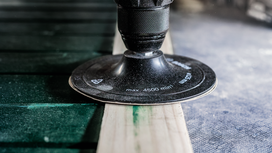 A rotary sander smooths the surface of a wooden plank.