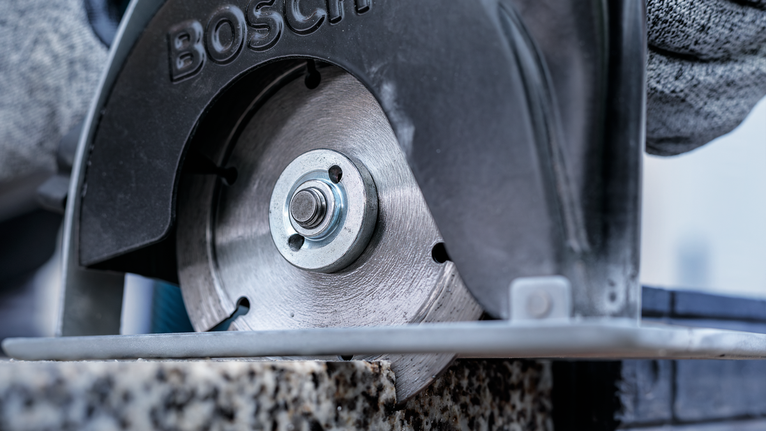 Person wearing safety equipment cuts stone with a circular saw.