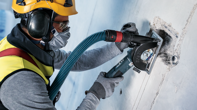 A person wearing safety equipment cuts into a concrete wall with a power tool.