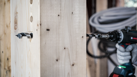 Person wearing safety equipment drills a hole through thick wooden beams.