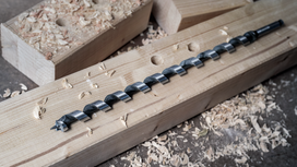 Long drill bit on a wooden beam surrounded by wood shavings.