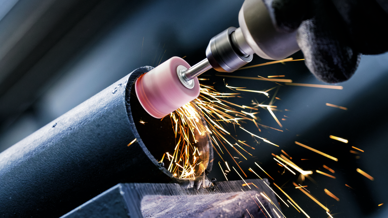PRO Steel Mounted Point Set, 25 x 24; 15 x 30; 15 x 30; 25 x 25; 20 x 25 mm, G60; G60; G60; G60; G60, 5 pcs Person wearing safety equipment grinds a metal pipe, creating bright sparks.