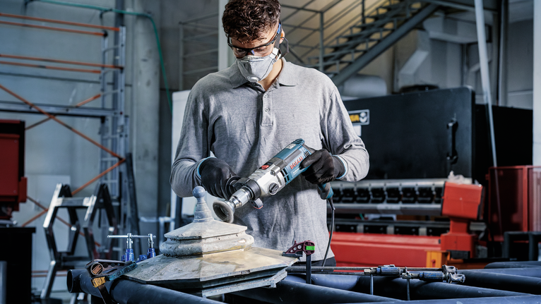 PRO Metal clean Cup Brush, Straight Shank, 70 x 0.3 mm Person wearing safety equipment drills into a metal fixture in an industrial workshop.