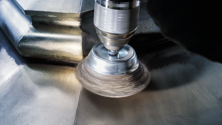 PRO Metal clean Cup Brush, Straight Shank, 70 x 0.3 mm A person wearing safety equipment polishes a metal surface with a rotary tool.