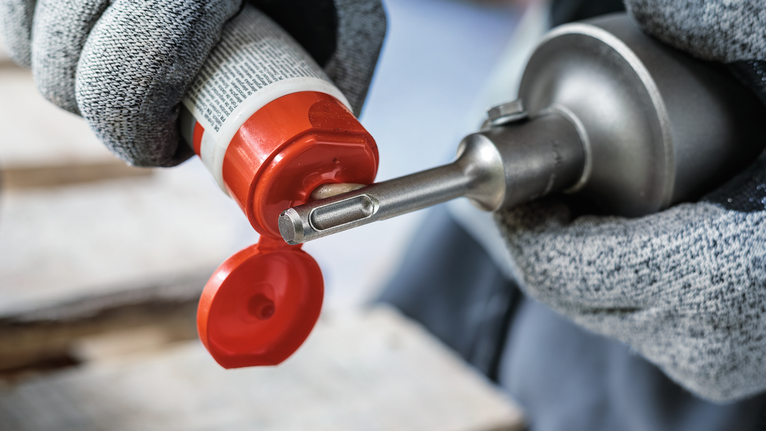 PRO SDS Shank Grease, for Drill and Chisel Person wearing safety equipment applies lubricant to a drill bit.