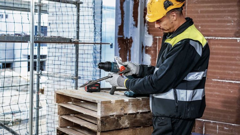 PRO SDS Shank Grease, for Drill and Chisel A person wearing safety equipment adjusts a cordless drill at a construction site.