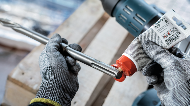 PRO SDS Shank Grease, for Drill and Chisel A person wearing safety equipment applies lubricant to a drill bit.