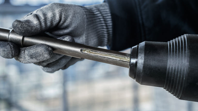 PRO SDS Shank Grease, for Drill and Chisel Person wearing safety equipment inserts a metal drill bit into a power tool.