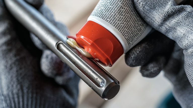 PRO SDS Shank Grease, for Drill and Chisel Person wearing safety equipment applies lubricant to a metal tool.
