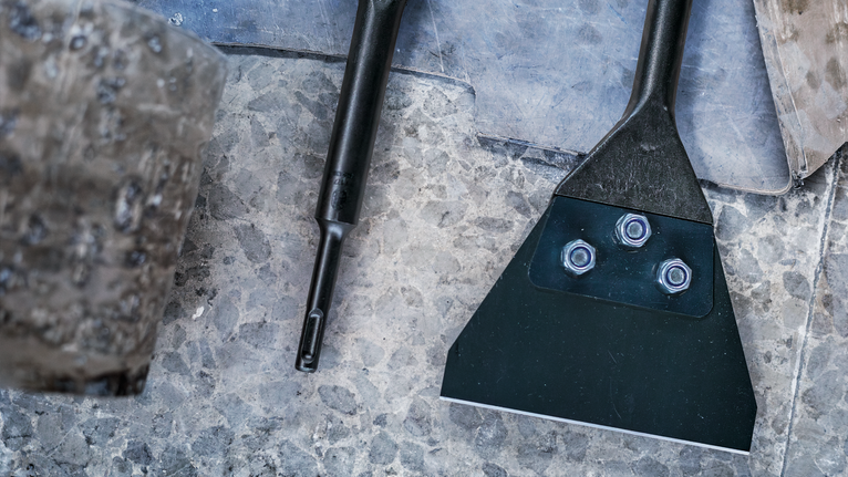 Wide metal chisel with bolts placed on a textured stone surface.